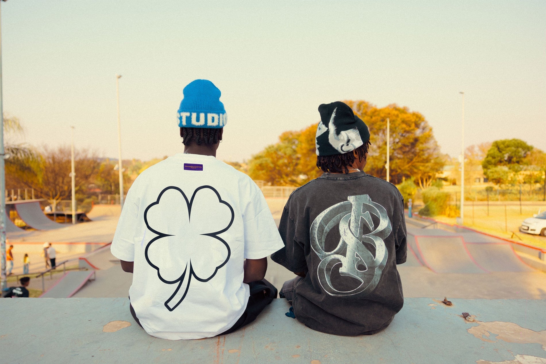 Two people wearing graphic oversized t-shirt styles while sitting beside a skate park.